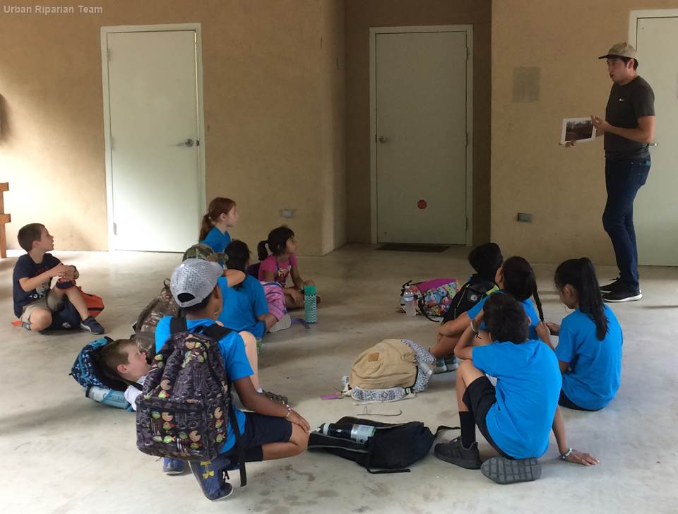 Urban riparian team presenting about stream restoration site to children at the Irma Lewis Seguin Outdoor Learning Center camp.